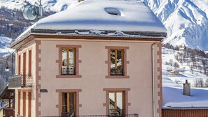 A pink building with a snow-covered roof, windows, and a balcony.