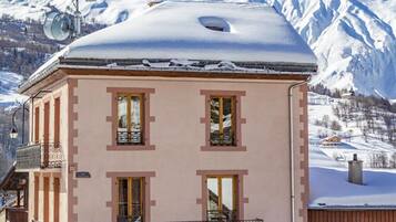 Un bâtiment rose, avec un toit, des fenêtres et un balcon couverts de neige.
