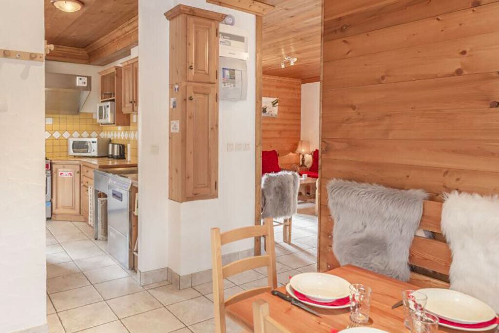 Un intérieur en bois comprenant un coin repas, une cuisine et un fauteuil rouge agrémenté d’un plaid en fourrure.