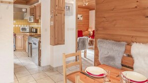 A wooden interior with a dining area, kitchen, and a red chair with a fur throw.