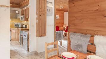 Un intérieur en bois comprenant un coin repas, une cuisine et un fauteuil rouge agrémenté d’un plaid en fourrure.