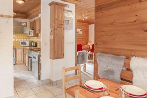 Interior em madeira com área de jantar, cozinha e uma cadeira vermelha com manta de pele.