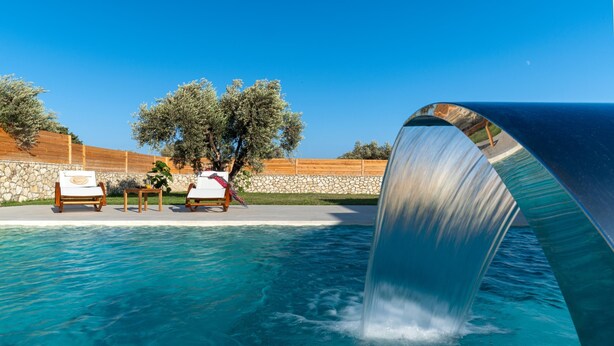 Une piscine agrémentée d’une cascade, de chaises longues et d  ’un mur de pierre orné d’arbres.