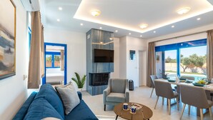 Ein modernes Wohnzimmer mit einer Couch, einem Esstisch mit Stühlen, einem an der Wand befestigten Fernseher und einem großen Fenster mit Blick.