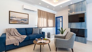 Ein modernes Wohnzimmer mit Sofa, Sessel, Couchtisch und einem wandmontierten Flachbildfernseher.