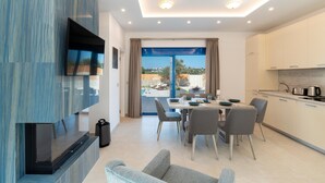 Ein modernes Wohnzimmer mit Flachbildfernseher, einem Essbereich mit Tisch und Stühlen sowie einer Küche mit Schränken und Geräten.
