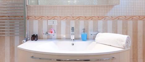 A bathroom with a large oval sink, a mirror above it, and a towel on the right. There are toiletries on the sink and a decorative tile border.