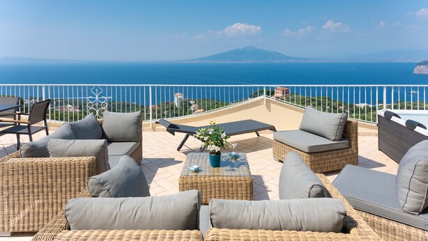 A terrace with wicker furniture and a view of the sea and a mountain.