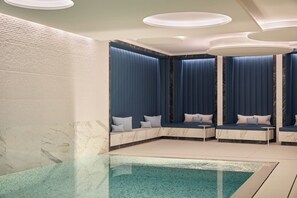 A modern spa room with a marble wall, a pool, and seating areas with blue curtains and cushions.