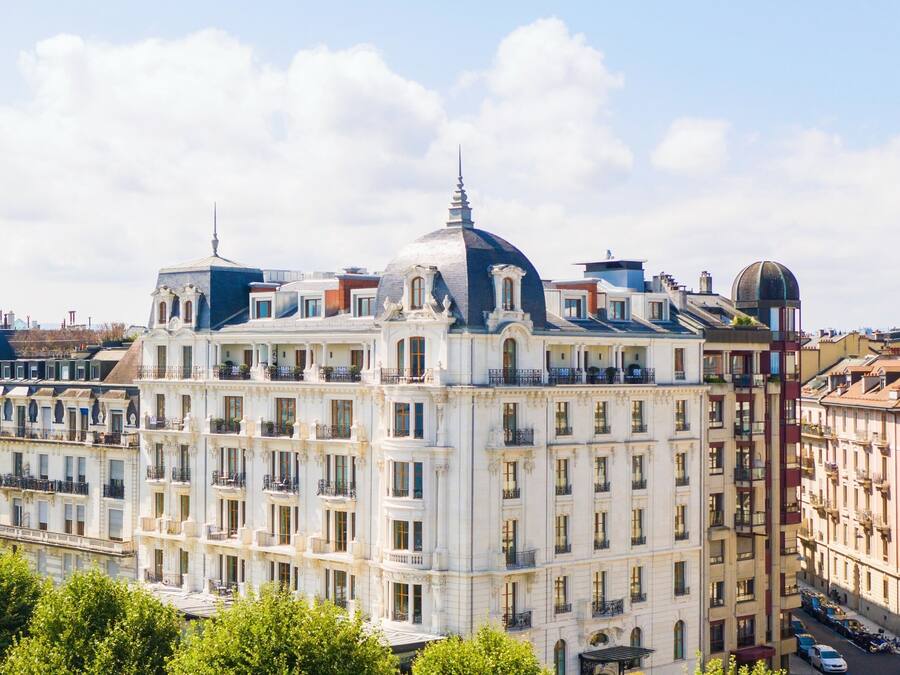 Un grand bâtiment historique, doté de nombreux étages et de balcons, entouré d’arbres et d’autres bâtiments.