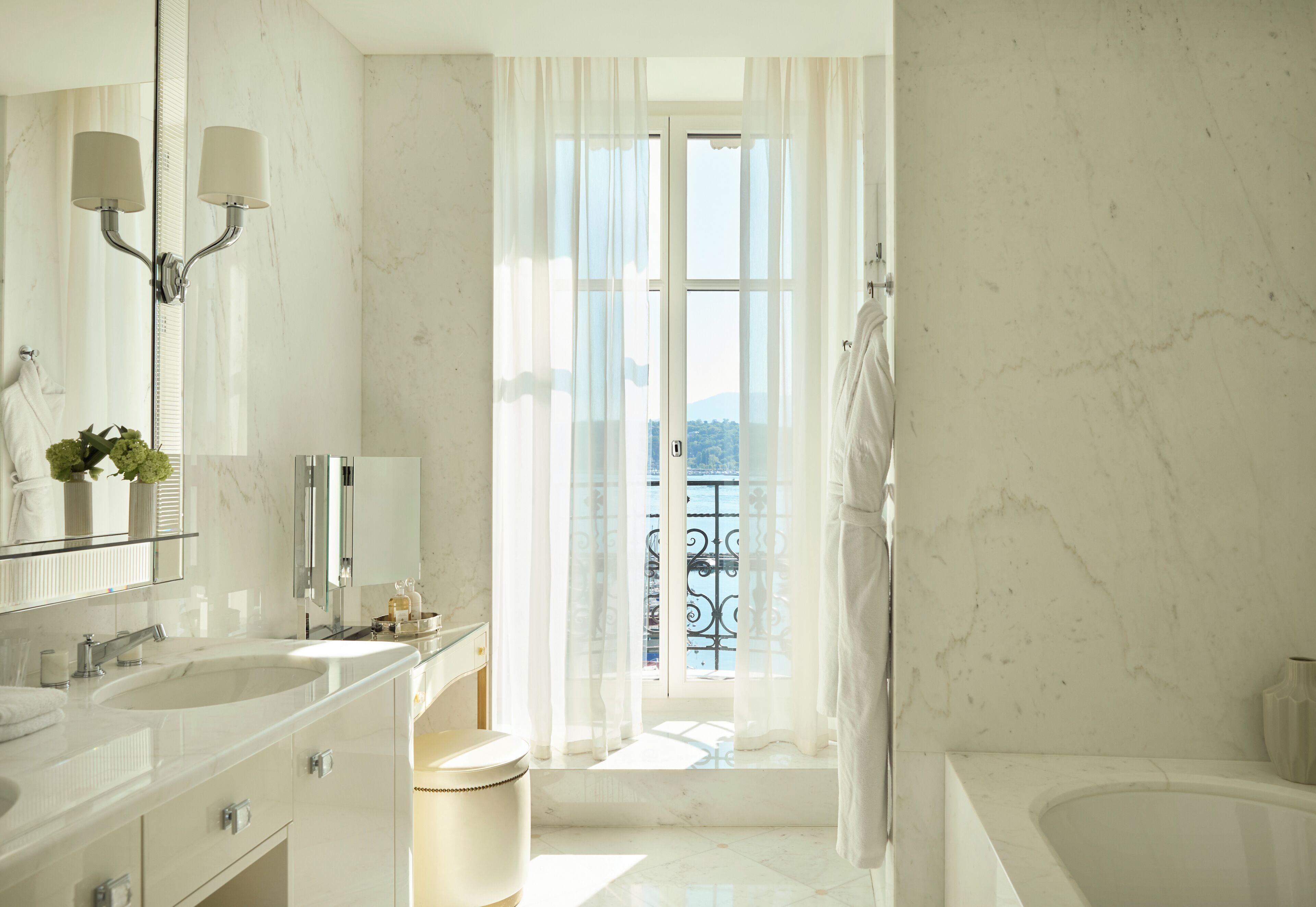 A modern bathroom with a large mirror, two sinks, a bathtub, and a view of a balcony with a railing.