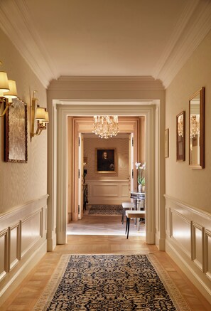 A hallway with a patterned rug, a chandelier, and framed artwork on the walls.