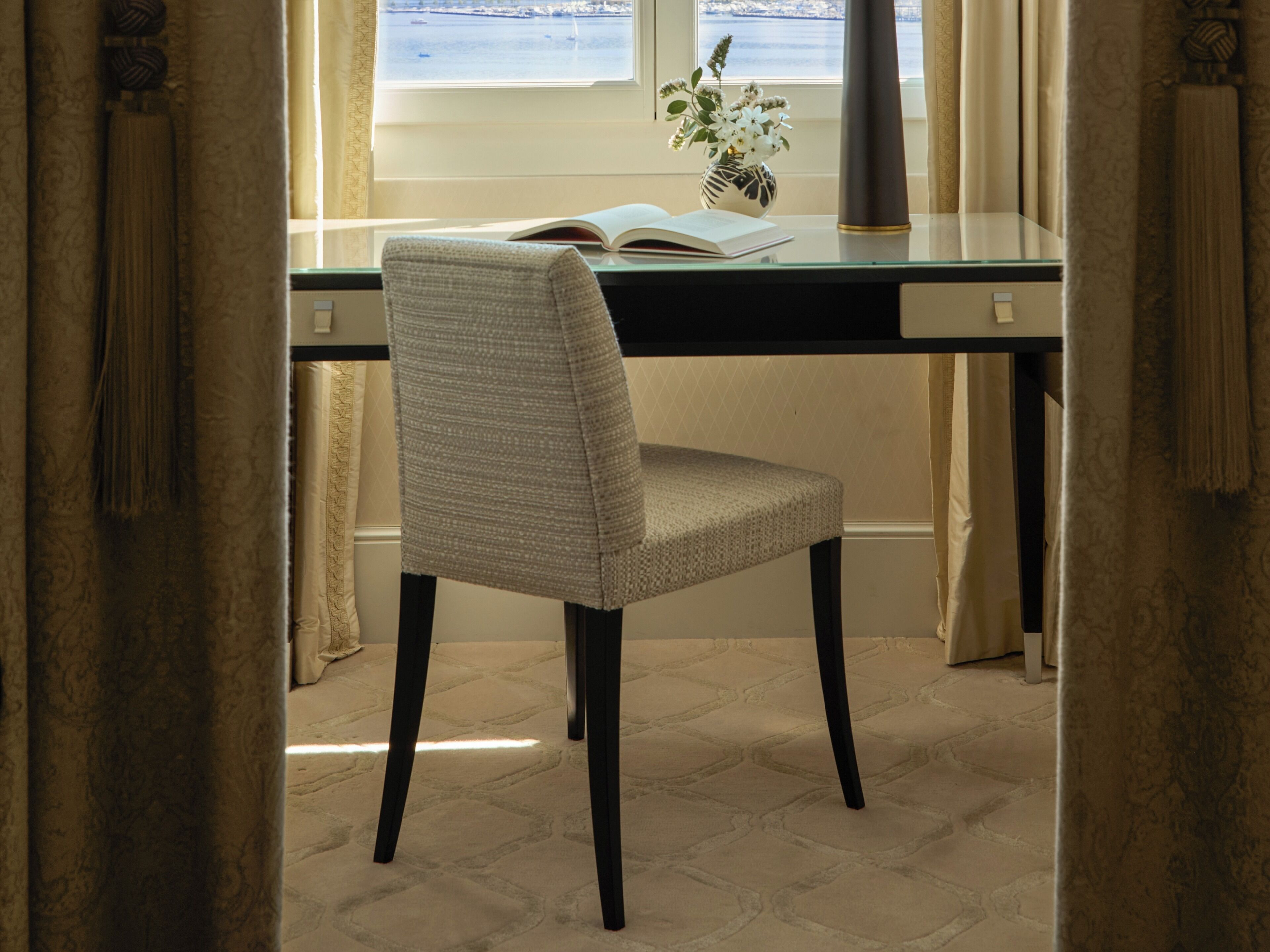 A study with a chair, a book, a vase with flowers, and a view of the sea through a window.