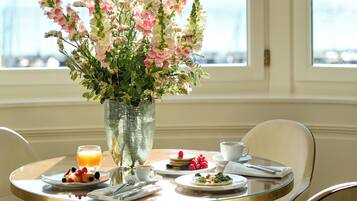 A dining table with a floral arrangement, breakfast items, and a view of the outdoors.