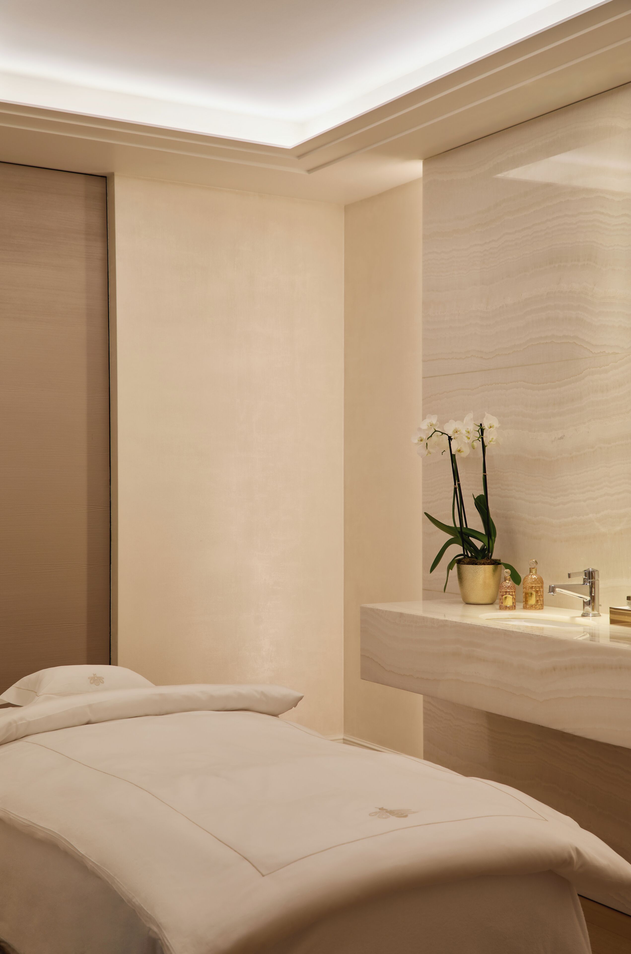 A modern bathroom with a large mirror, a sink with toiletries, and a potted orchid.