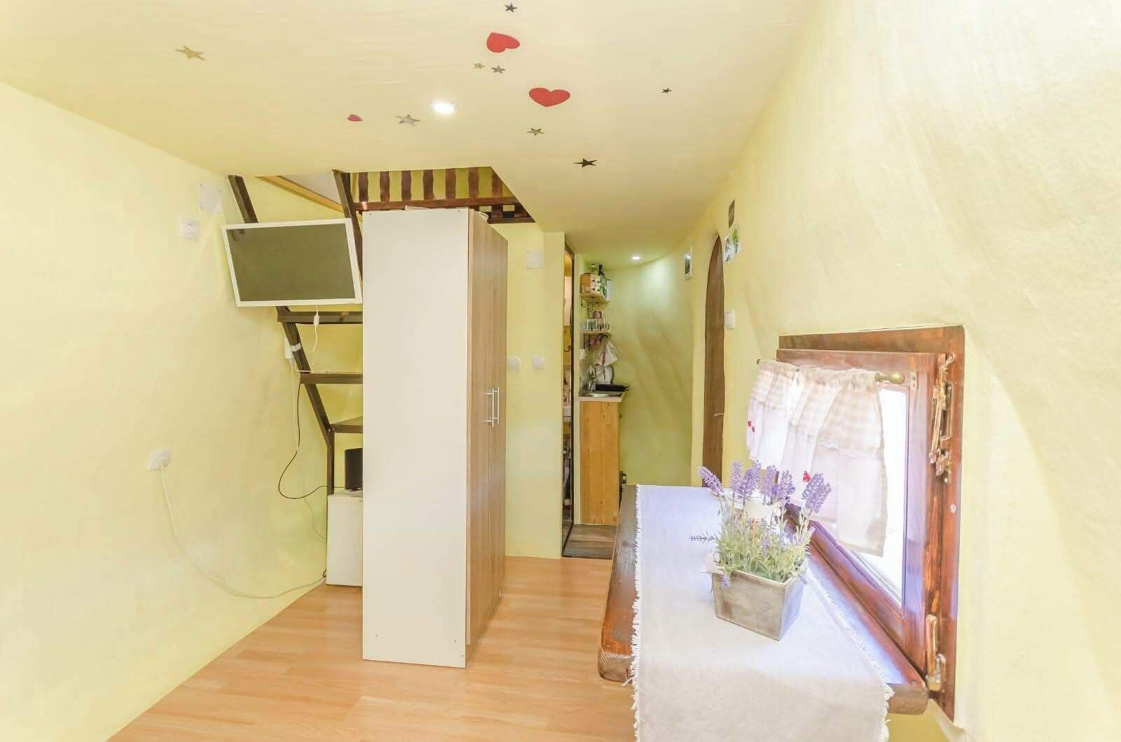 Un pasillo estrecho con una escalera de madera, una puerta blanca y una pequeña mesa con un jarrón de flores.