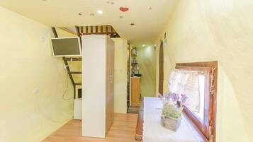 Un pasillo estrecho con una escalera de madera, una puerta blanca y una pequeña mesa con un jarrón de flores.