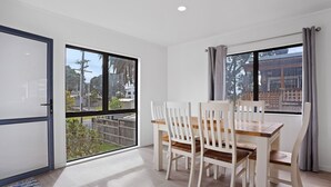 A dining area with a table and chairs, large windows with curtains, and a view of the outside.