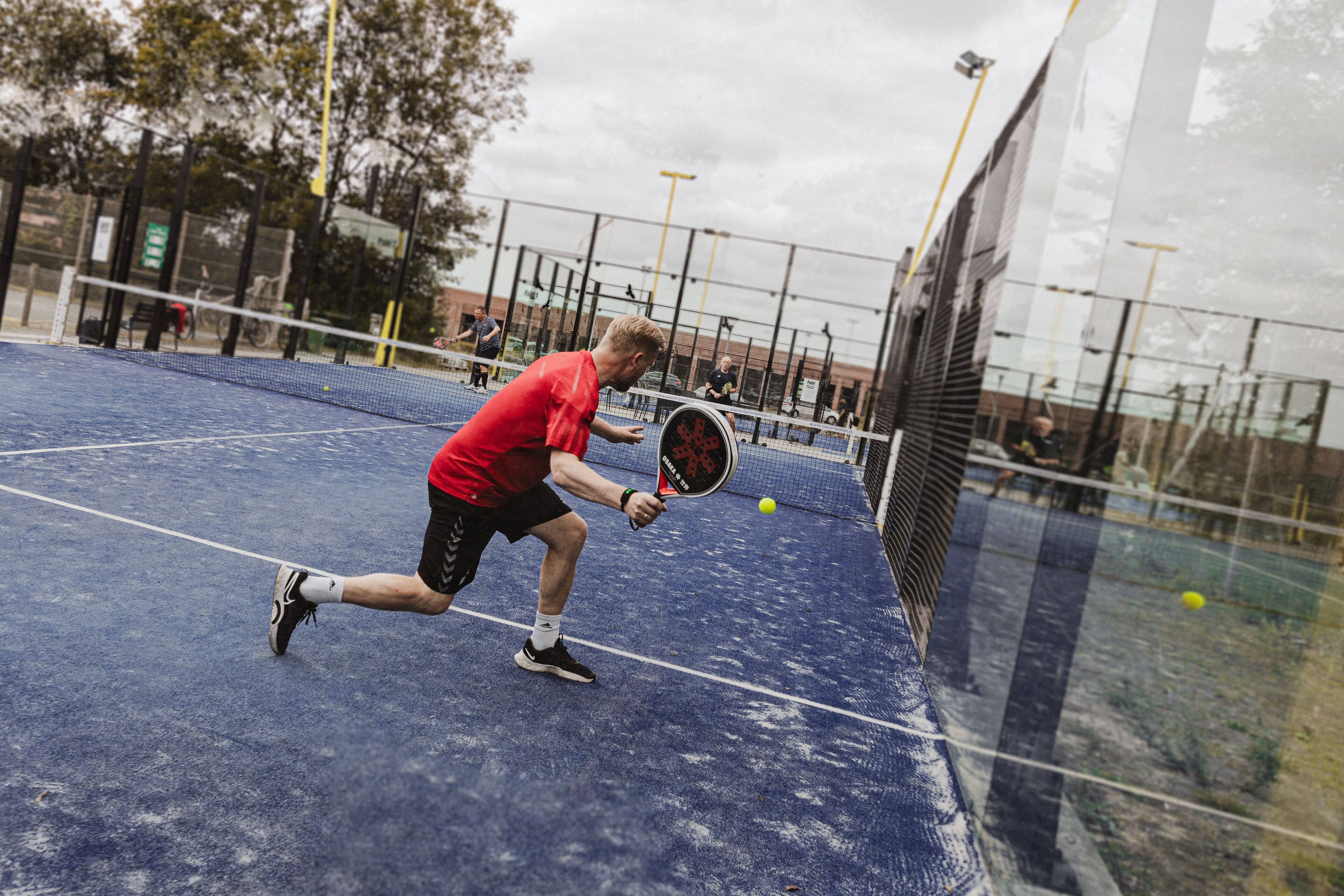 A tennis court with a net, a player in a red shirt, and a tennis ball in motion.
