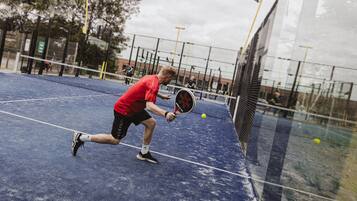 A tennis court with a net, a player in a red shirt, and a tennis ball in motion.