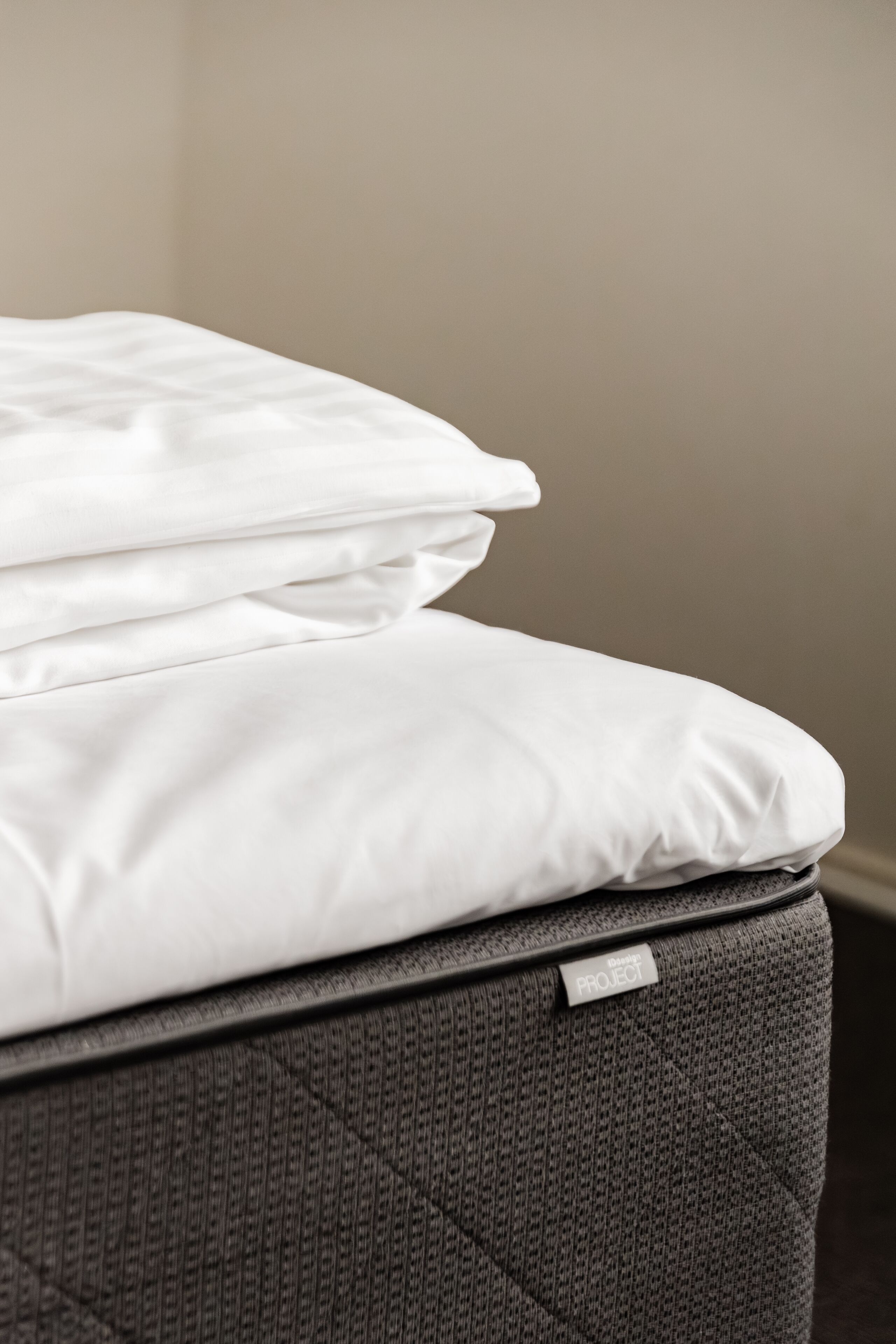 A neatly made bed with white bedding and a gray upholstered headboard.