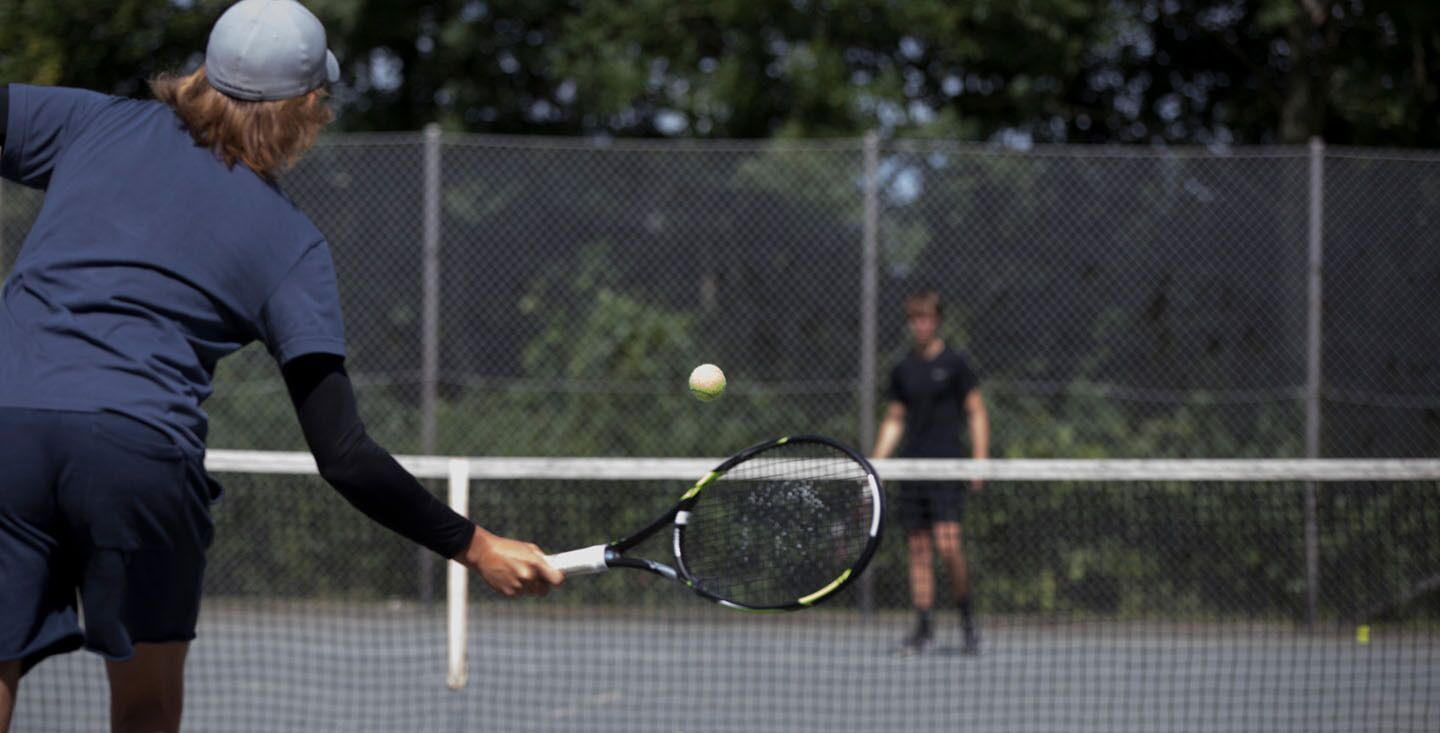A tennis court with a net in the center, surrounded by a fence.