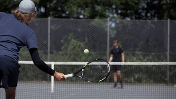 A tennis court with a net in the center, surrounded by a fence.