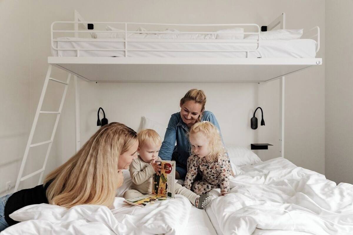 A bunk bed room with a ladder, a bedside table, and a wall-mounted lamp.