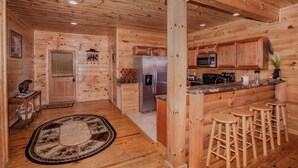 Interior de uma cabana de madeira com cozinha, incluindo geladeira, micro-ondas e banquetas.