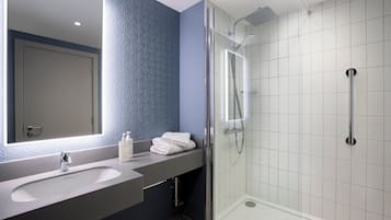 A modern bathroom with a large mirror, two sinks, and a shower area.