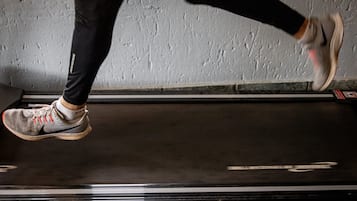 A person running on a treadmill in a room with a textured wall.