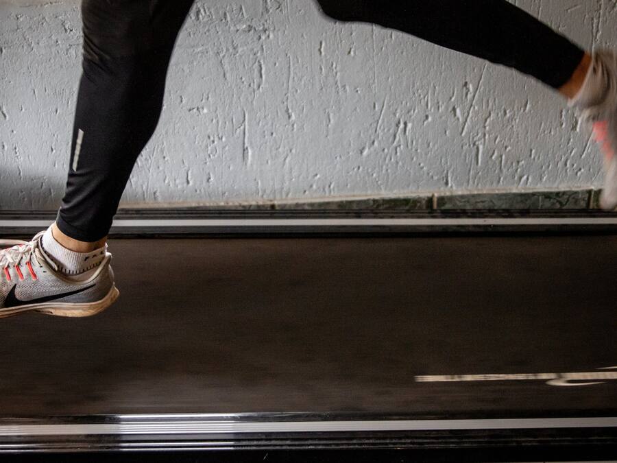 A person running on a treadmill in a room with a textured wall.