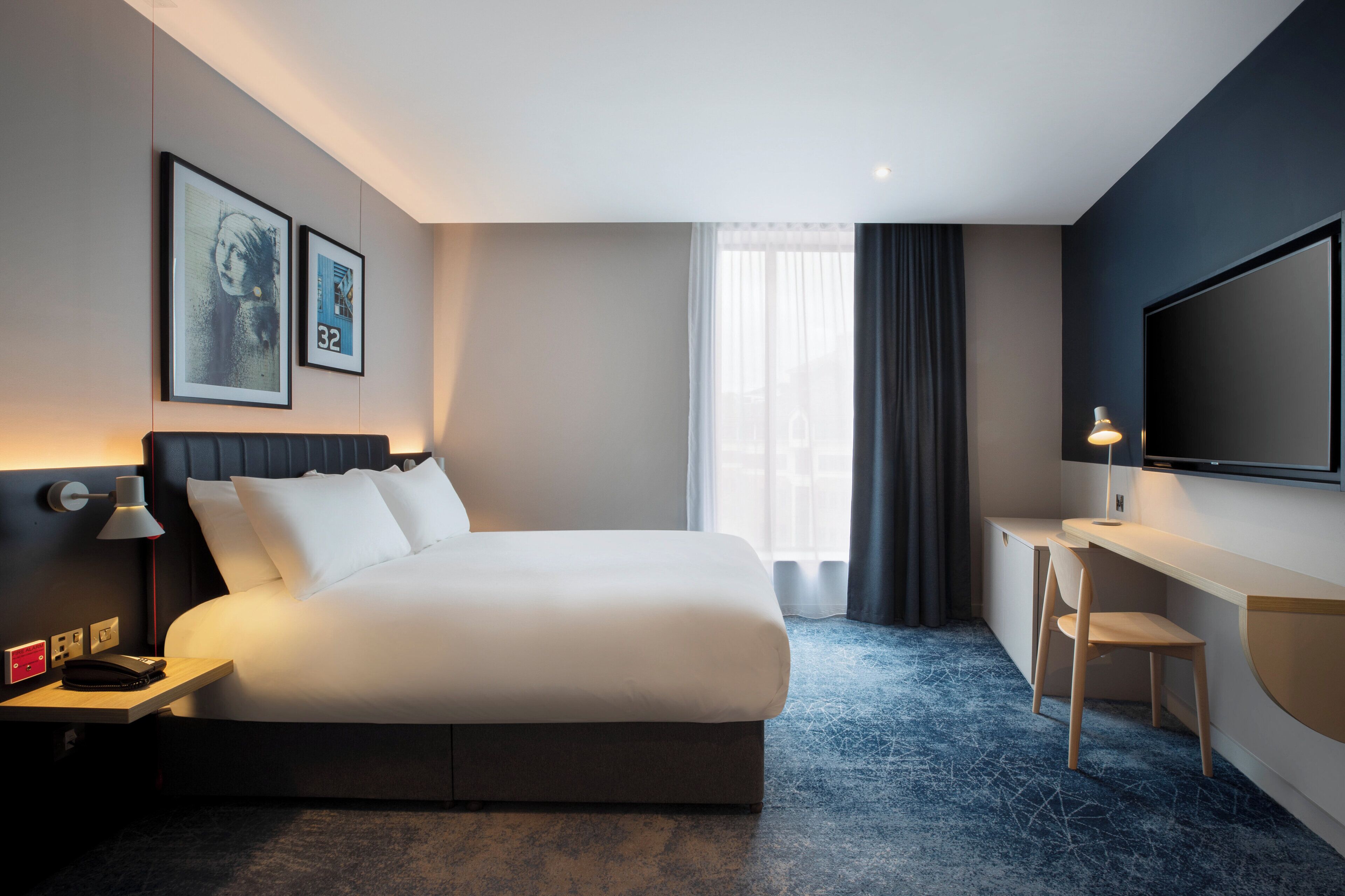 A modern hotel room with a large bed, a desk, and a TV.