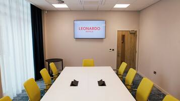 Un salón de conferencias con una larga mesa, sillas amarillas, una pantalla que muestra 'LEONARDO HOTELS' y una puerta.