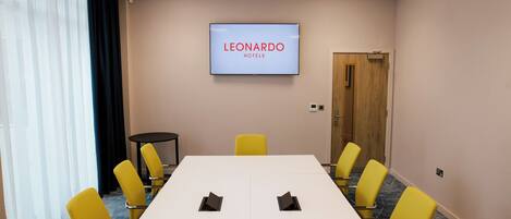 Un salón de conferencias con una larga mesa, sillas amarillas, una pantalla que muestra 'LEONARDO HOTELS' y una puerta.
