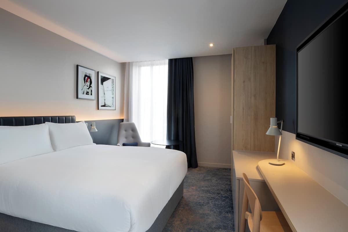 Quarto de hotel moderno com uma cama grande, uma escrivaninha, uma cadeira e uma televisão.