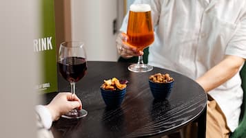 A person holding a glass of beer at a table with two bowls of snacks.