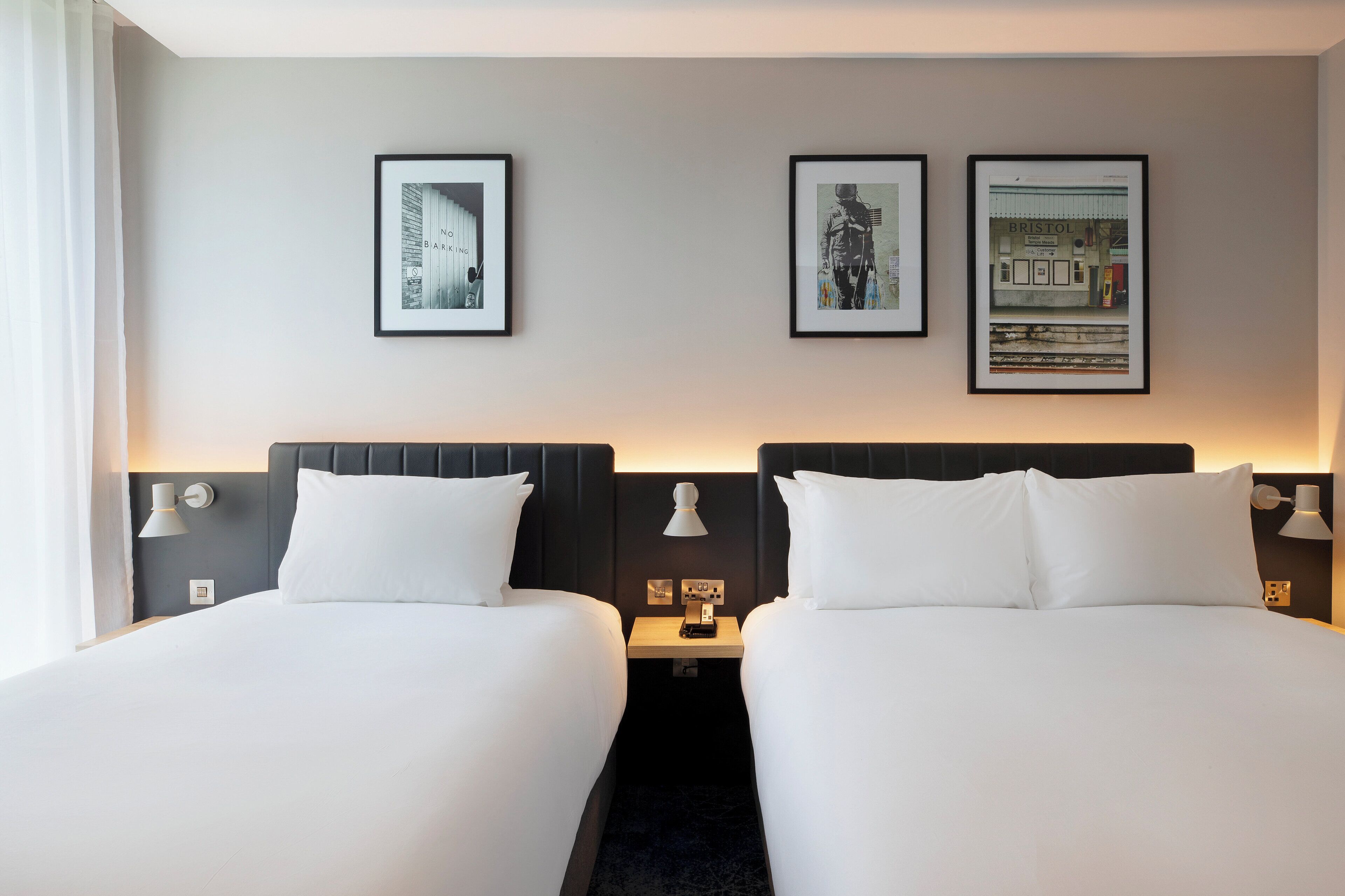 A hotel room with two beds, a nightstand with a lamp, and three framed pictures on the wall.
