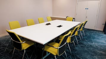 A conference room with a white table, yellow chairs, a blue carpet, and a white door with a blue lock.