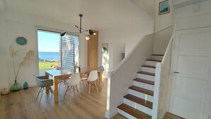 Une pièce spacieuse avec un plancher en bois, une table à manger avec des chaises, un escalier et une vue sur la mer.