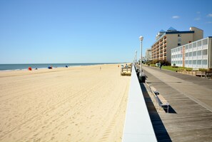 Ein Strand mit einem Holzsteg, einem Gebäude mit großen Fenstern und einem klaren Himmel.
