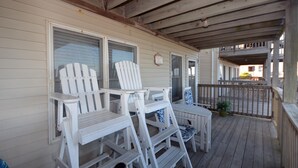 Eine überdachte Veranda mit weißen Adirondack-Stühlen, einem kleinen Tisch, einem Holzboden und einem Geländer.