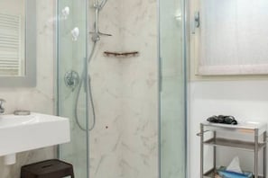 A bathroom with a glass shower enclosure, a white sink, and a small shelf with toiletries.