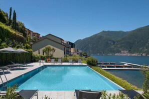 A swimming pool with lounge chairs, a lifebuoy, and a view of a lake and mountains.