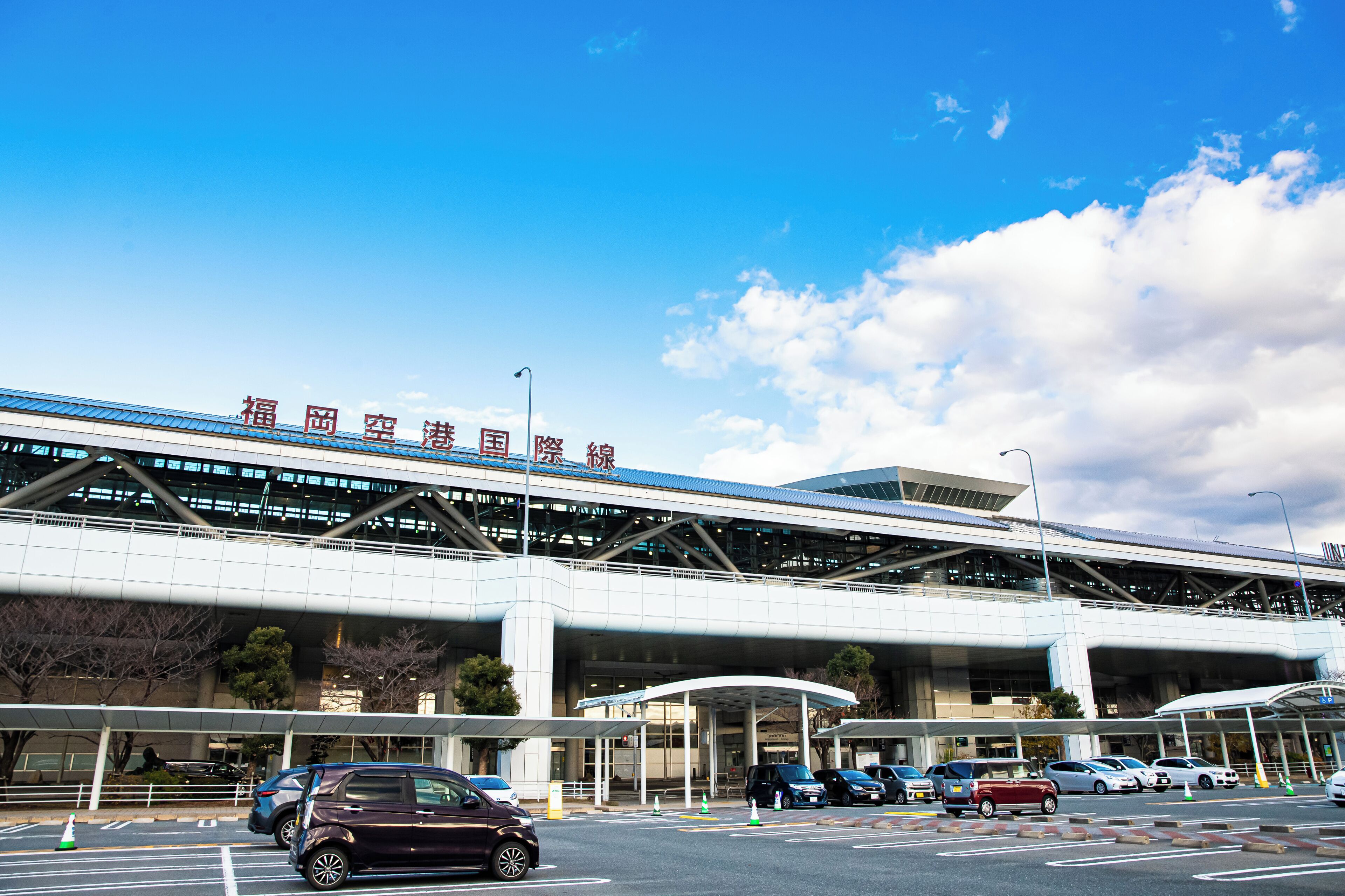 A modern airport terminal with clear signage, multiple entry points, and a covered waiting area.