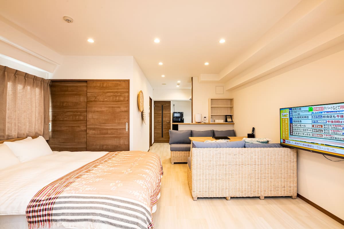 A hotel room with a large bed, a sofa, a small table, and a TV on the wall.