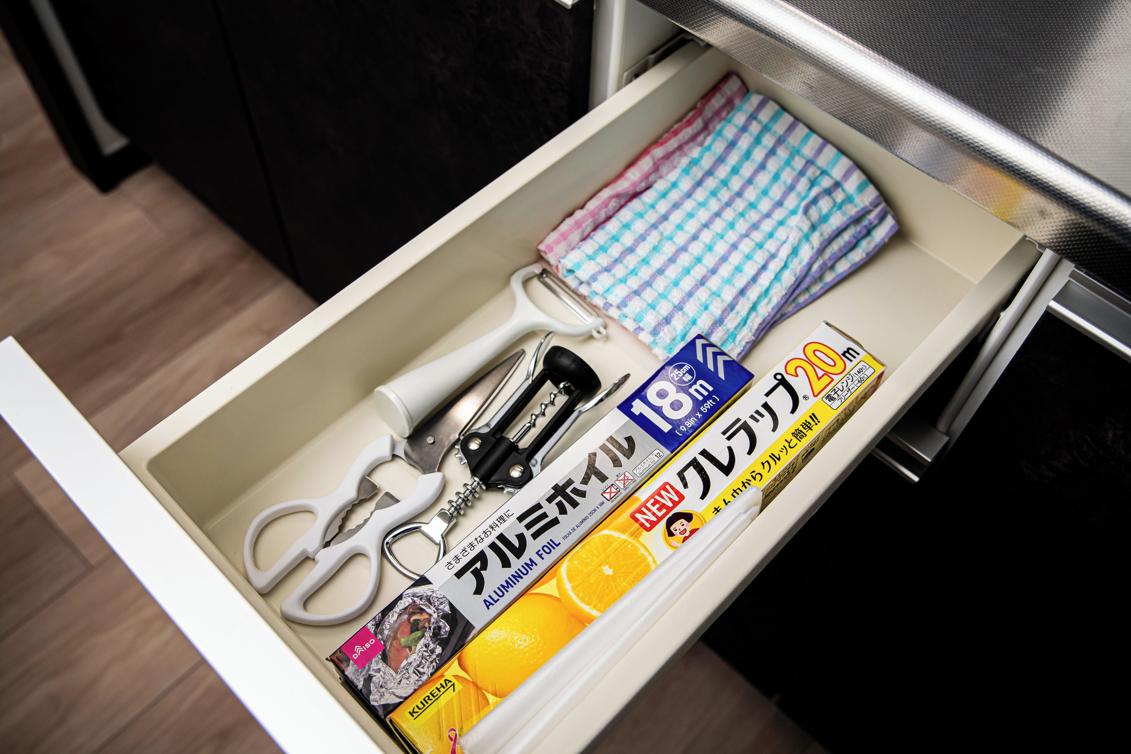 A drawer containing a pair of scissors, a cleaning cloth, a can opener, and a box of aluminum foil.