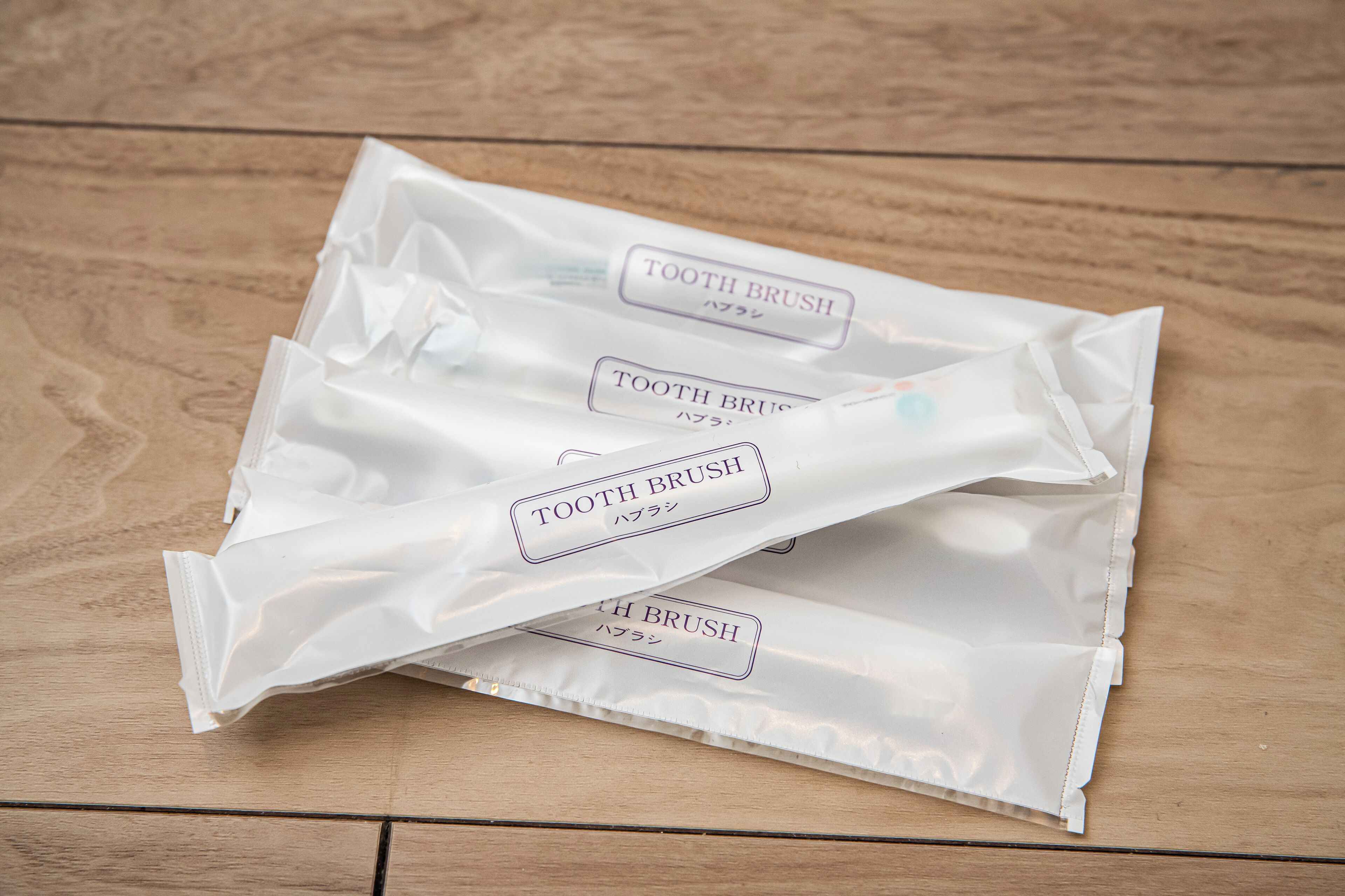 Tre confezioni bianche etichettate 'TOOTH BRUSH' su un ripiano di legno.