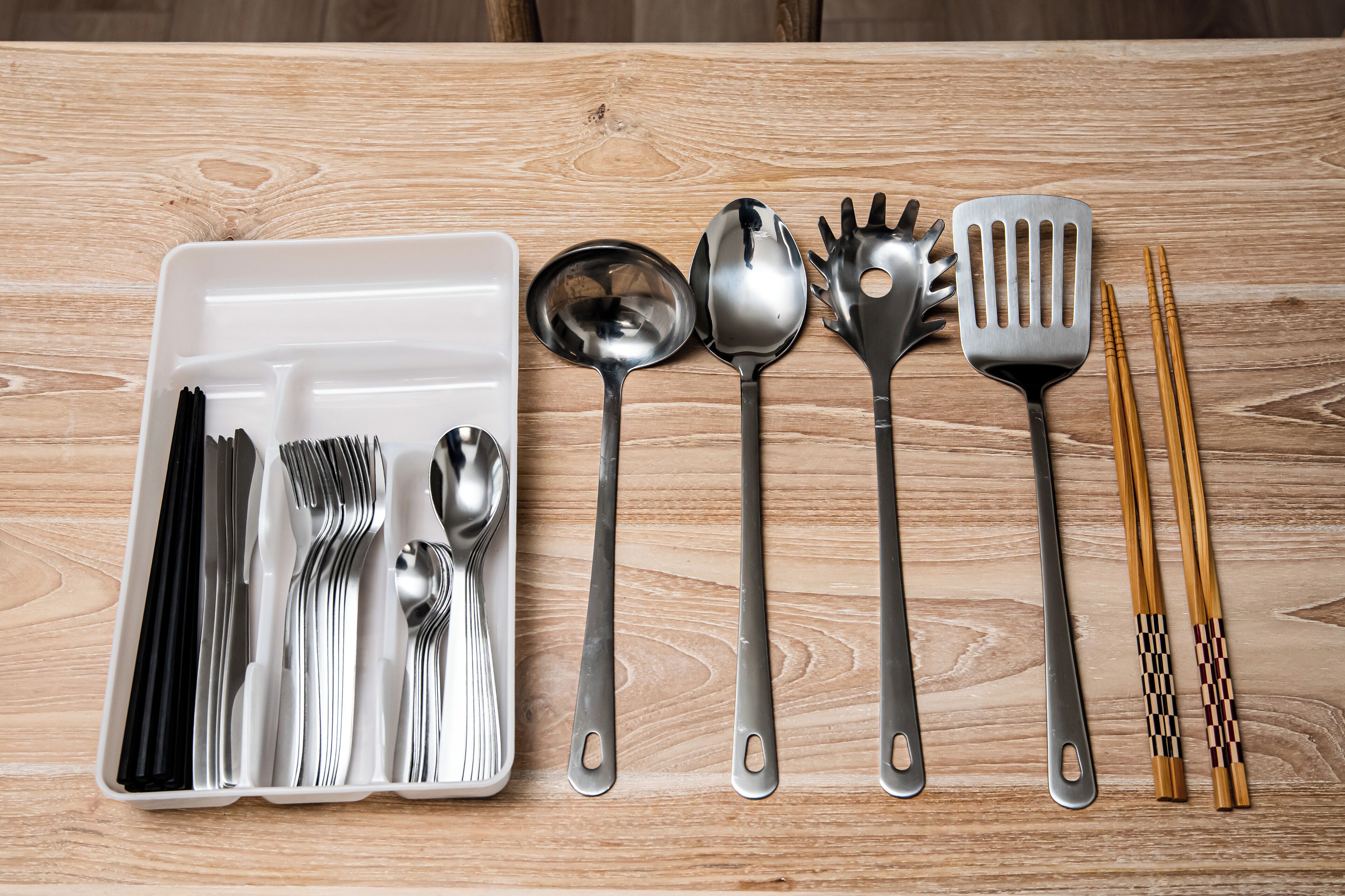 Uma mesa de madeira com diversos utensílios de cozinha, incluindo colheres, garfos, uma espátula e palitos.