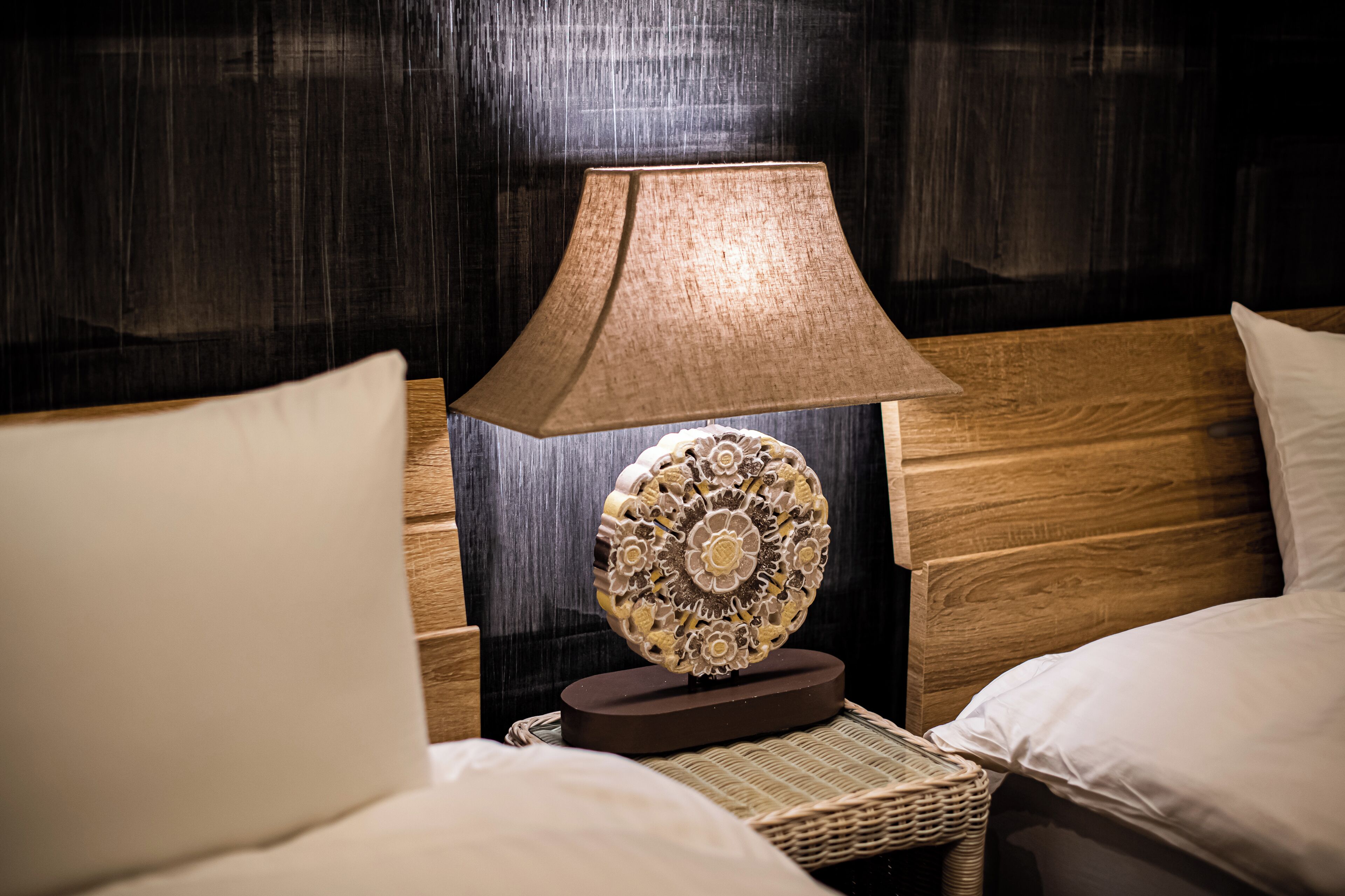 A neatly made bed with a wooden headboard, a decorative wall hanging, and a lamp on a bedside table.